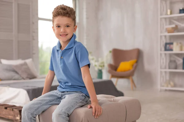 Pequeno menino bonito sentado em hassock na sala de estar — Fotografia de Stock