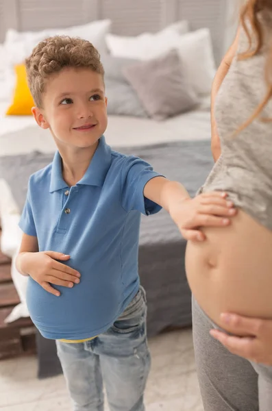 Curly bonito filho com bola debaixo da camisa brincando com a mãe grávida — Fotografia de Stock