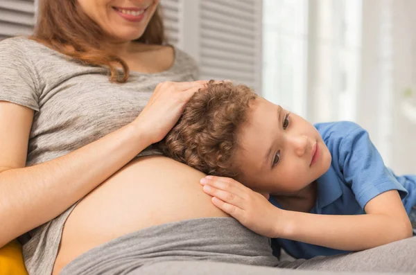 Dunkeläugiger hübscher Junge liegt auf Bauch seiner schwangeren Mutter — Stockfoto