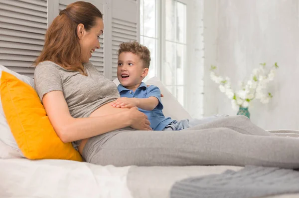 Lockiger neugieriger kleiner Junge lacht mit seiner schwangeren Mutter — Stockfoto