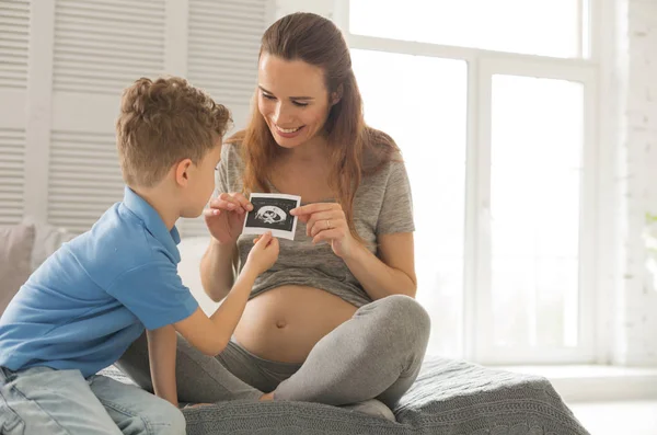 Filho pequeno encaracolado olhando para a investigação ultra-sonográfica da futura irmã — Fotografia de Stock