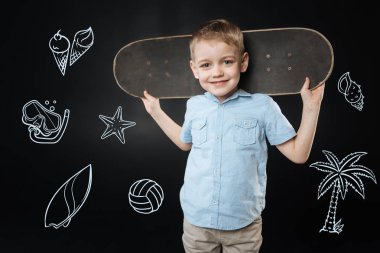 Gülümseyen ve bir kaykay başının arkasına tutan duygusal çocuk