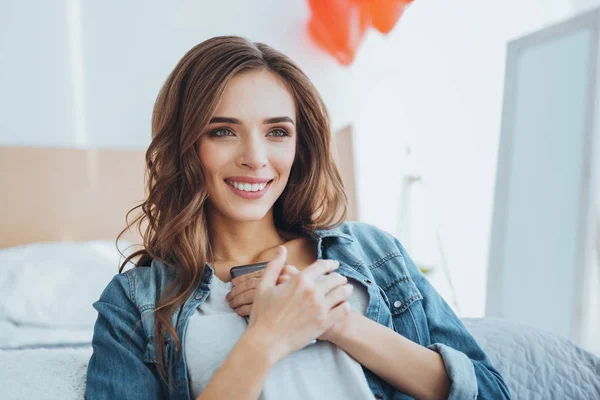 Encantada mujer feliz presionando su teléfono inteligente en el pecho —  Fotos de Stock