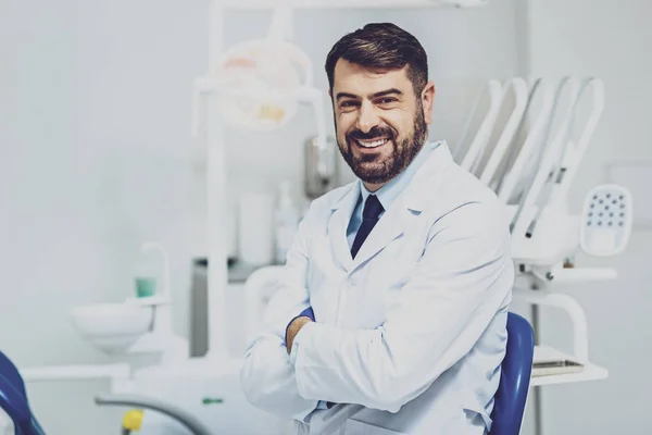 Positive delighted dentist sitting at his workplace — Stock Photo, Image