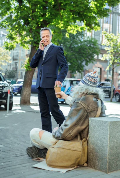 Hombre de negocios exitoso ayudando a personas sin hogar mientras habla por teléfono —  Fotos de Stock