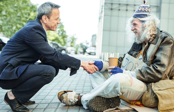 Улыбающийся добрый бизнесмен пожимает руку голодающему человеку — стоковое фото