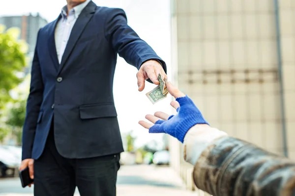 Trabalhador de colarinho branco dando nota de dólar para vagabundos sem-teto — Fotografia de Stock