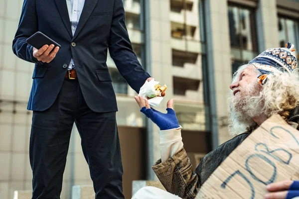 Sorrindo sem-teto homem tomando hambúrguer de coração bondoso estranho — Fotografia de Stock