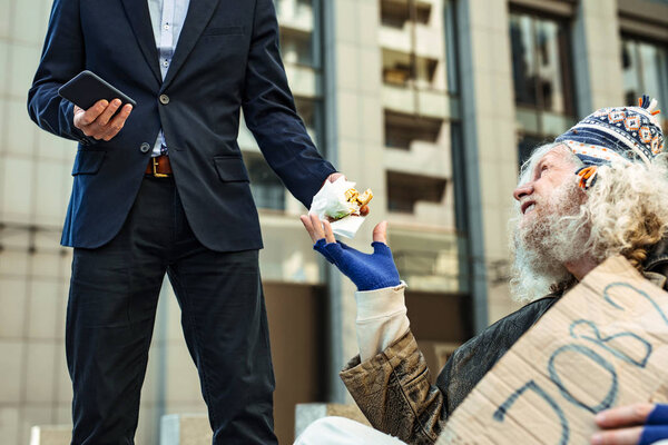 Smiling homeless man taking burger from kind-hearted stranger