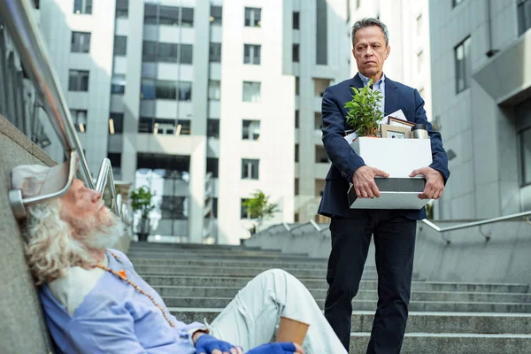 Fired man leaving office seeing homeless man — Stock Photo, Image