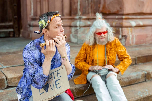 Man wearing shining jacket and floral headband playing the harmonica