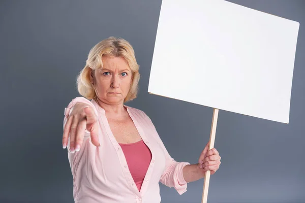 Mujer de mediana edad de pelo rubio sosteniendo pancarta y señalando — Foto de Stock