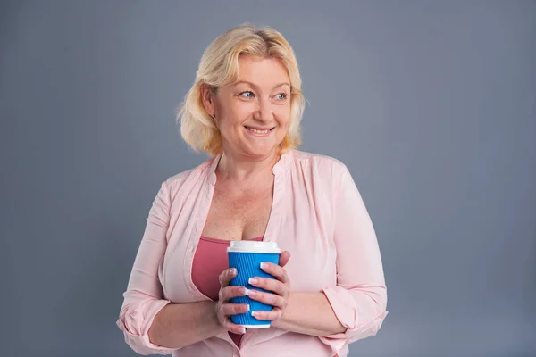Cheerful middle-aged woman holding blue coffee cup — Stock Photo, Image