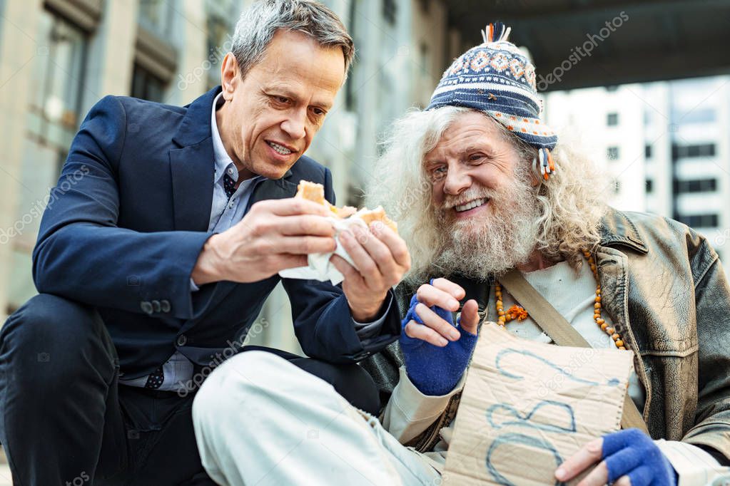 Smiling homeless elderly man eating burger from stranger