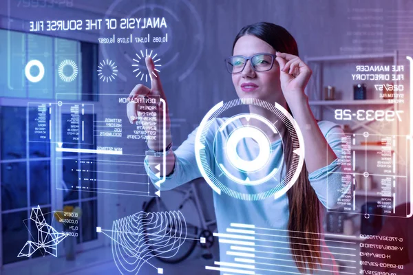 Mujer inteligente sonriendo y tocando sus gafas mientras mira la pantalla — Foto de Stock