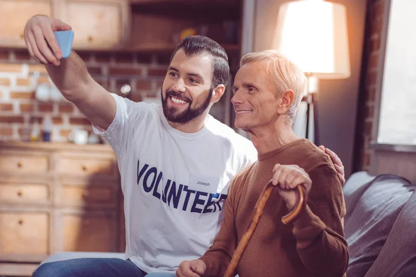 Позитивный восторженный доброволец сидит рядом с пенсионером — стоковое фото