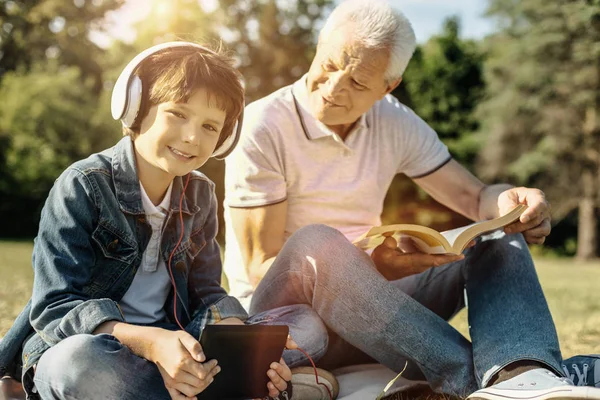 微笑男孩与他的平板电脑和耳机坐在爷爷 — 图库照片