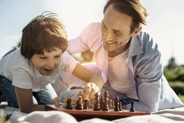 お気に入りのゲームです チェスをして自然を楽しんで彼のお父さんと彼のお父さんは笑顔でうれしそうな笑い折り敷き少年 — ストック写真