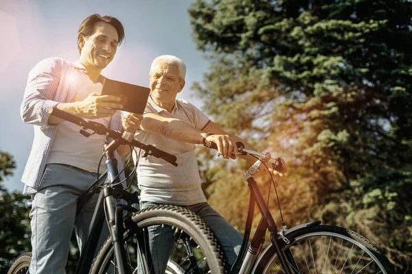 Hombre y su padre en bicicletas mirando una tableta —  Fotos de Stock