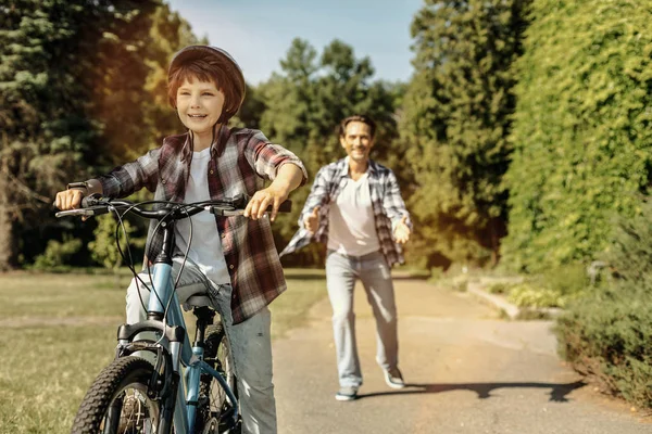 Chico montando su bicicleta y su padre corriendo — Foto de Stock