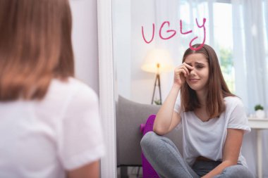 Upset teen girl believing in her ugliness clipart
