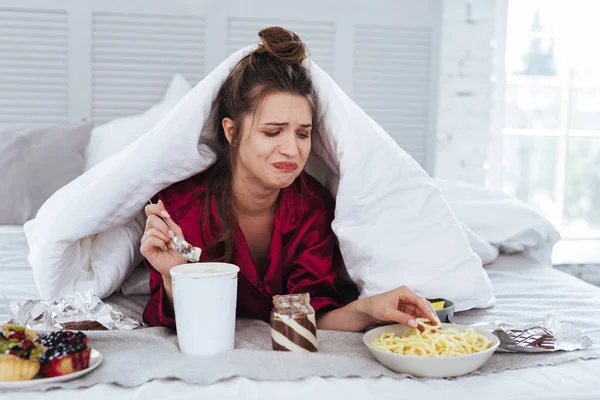 Mujer llorando acostada en su cama rodeada de bocadillos — Foto de Stock