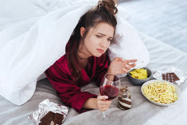 Stressad kvinna i baggy pyjamas holding glas vin — Stockfoto