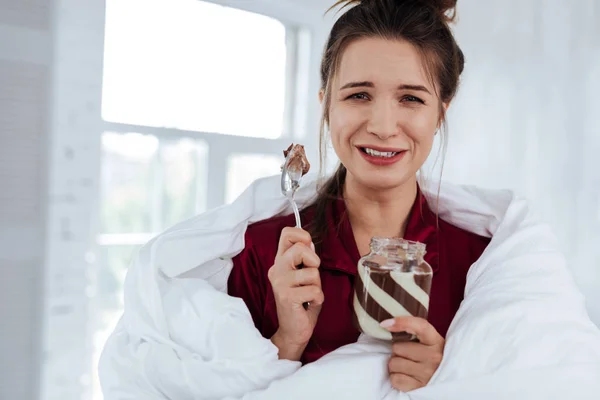 郁闷的女人吃巧克力的蔓延坐在床上 — 图库照片