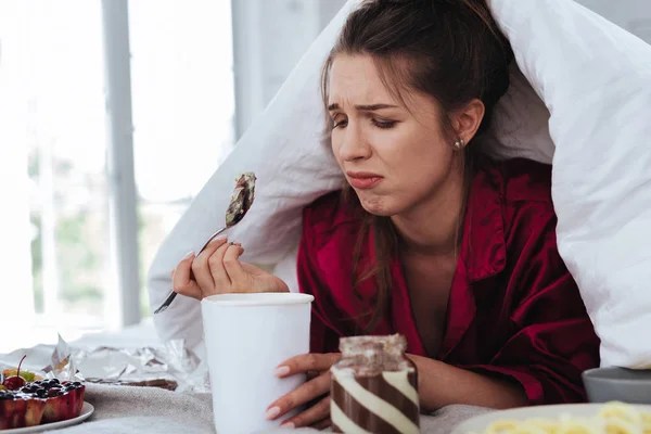 Stressed woman hiding under coverlet eating ice cream — Stock Photo, Image