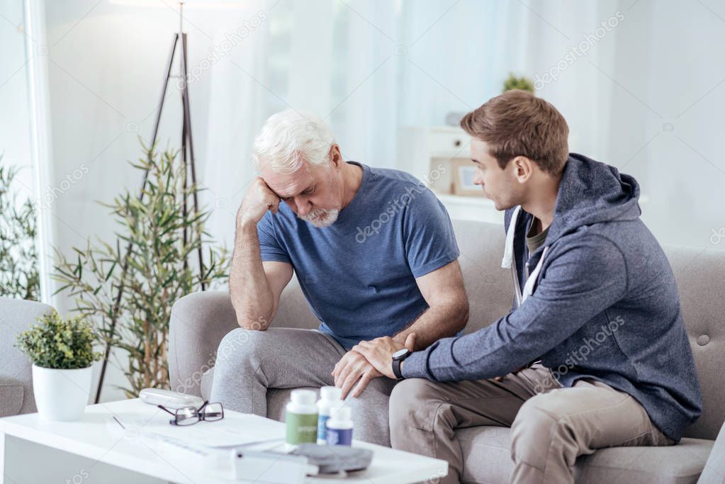 Worried male caregiver calming down senior man