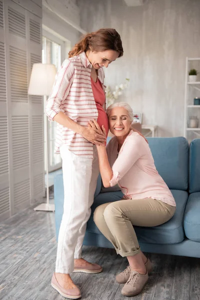 Extremt glad kvinna att placera hennes öra nära gravida mage — Stockfoto