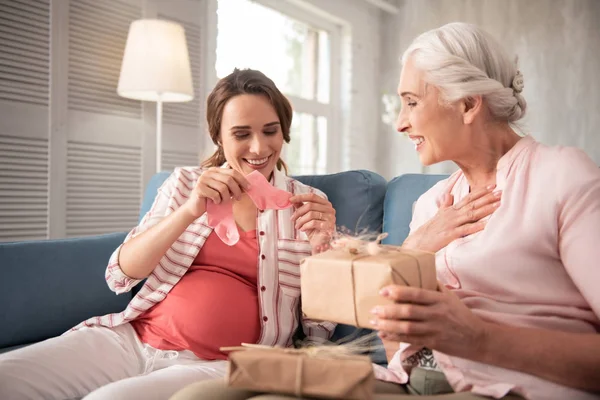 Loving mother presenting little pink socks to pregnant daughter — Stock Photo, Image