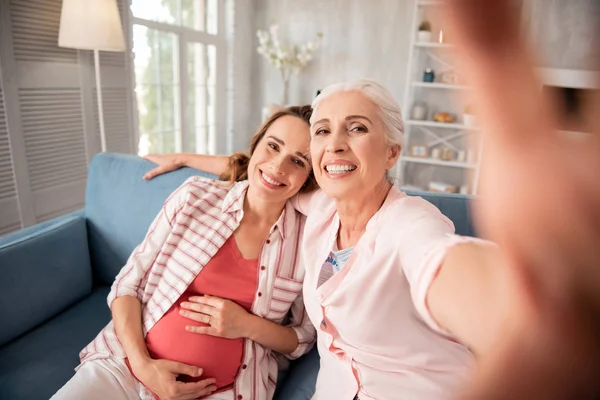 Dark-haired beaming woman making photo with her anticipating daughter — Stock Photo, Image