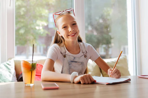 Beaming menina de olhos escuros desenho natureza sentado no café — Fotografia de Stock