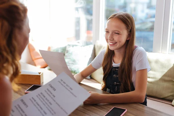 Blonde-haired girl smiling while choosing dish from menu