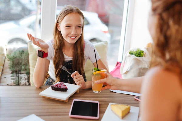 Улыбающаяся девушка ест десерт и пьет коктейль с мамой — стоковое фото