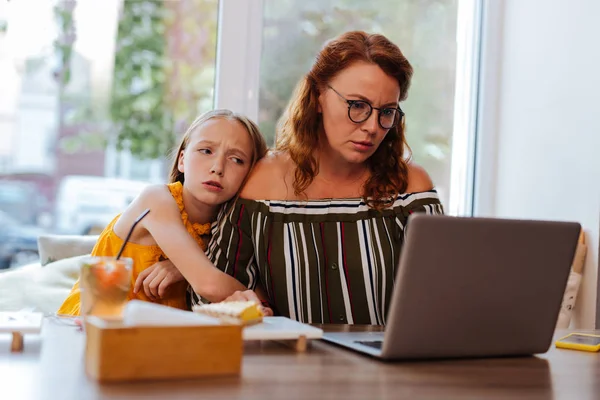 Bionda adolescente si sente annoiato seduto vicino alla madre che lavora — Foto Stock