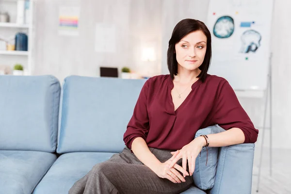 Ruhige junge Frau auf dem Sofa sitzend und nachdenklich lächelnd — Stockfoto