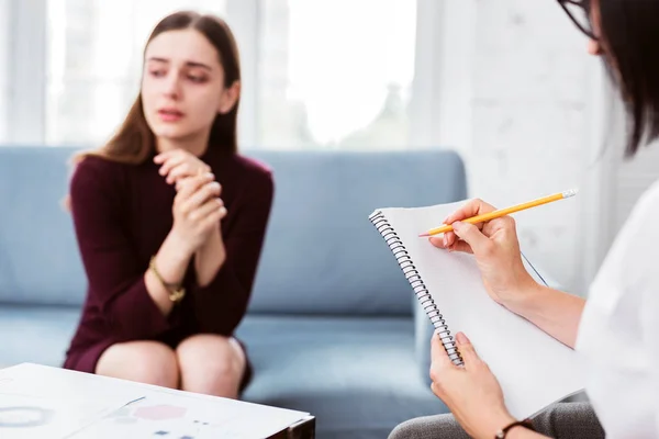 Vorsichtiger Arzt macht sich Notizen, während eine Patientin ihre Geschichte erzählt — Stockfoto