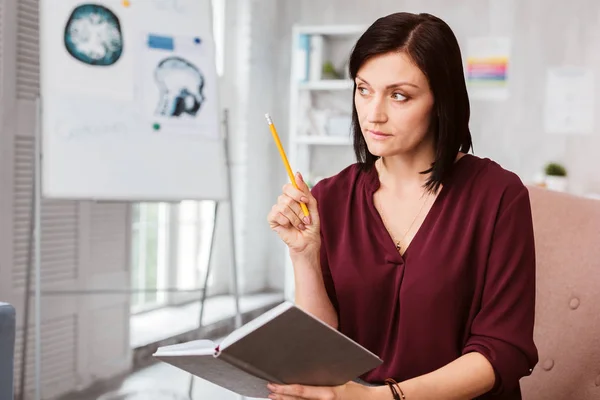 Serious neurologist holding a pencil and looking at her patient — Stock Photo, Image