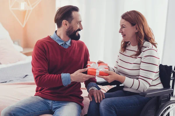 Mujer emocional en silla de ruedas sosteniendo un regalo y luciendo feliz — Foto de Stock