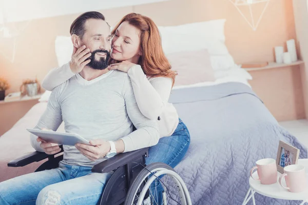 Milá žena při pohledu na svého manžela na invalidním vozíku a usmívá se — Stock fotografie