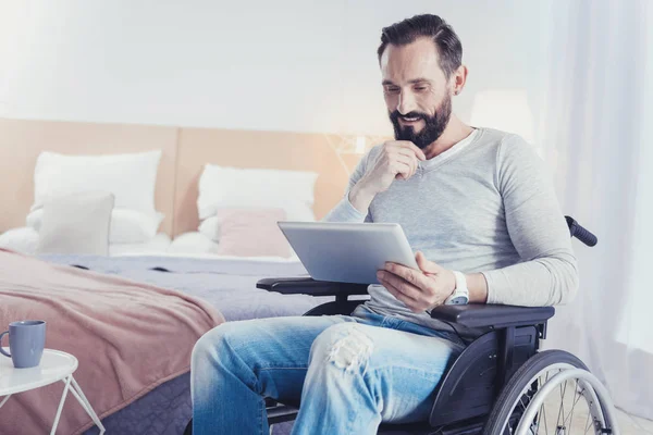 Умный блогер сидит в инвалидном кресле и смотрит на экран своего устройства — стоковое фото