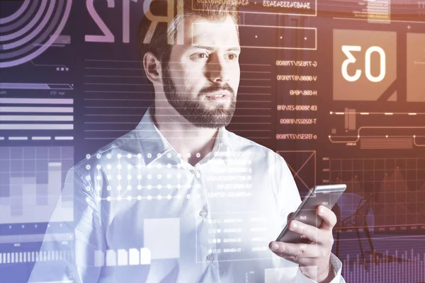 Bearded young man holding a smartphone and looking at the transparent computer — Stock Photo, Image
