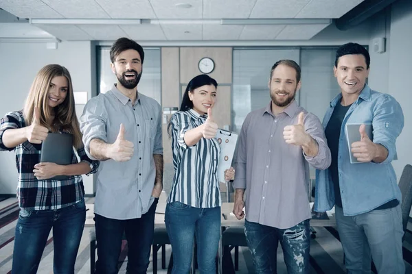 Cheerful smiling young colleagues thumbing up in the office — Stock Photo, Image