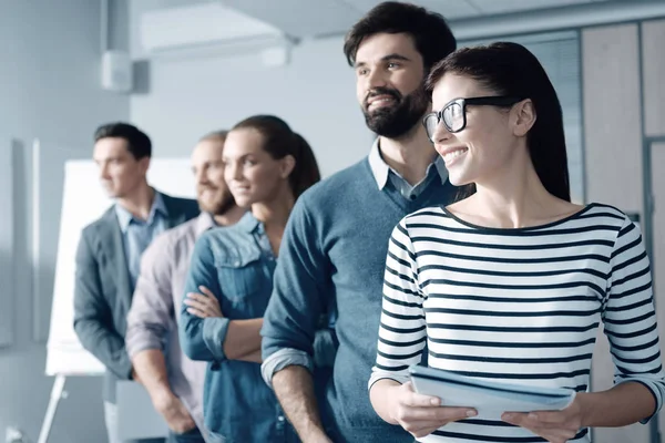 Mujer sonriente alegre de pie con sus colegas en la oficina — Foto de Stock