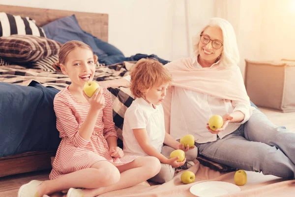 Smart barnbarn och deras tankeväckande mormor äta äpplen hemma — Stockfoto