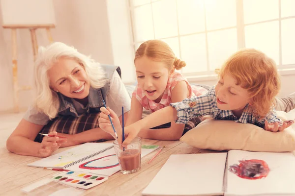 Gioioso pensionato signora guardando nipoti pittura insieme — Foto Stock