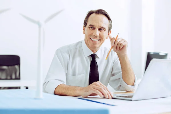 Elegantní usmívající se muž sedí s přenosným počítačem v kanceláři — Stock fotografie