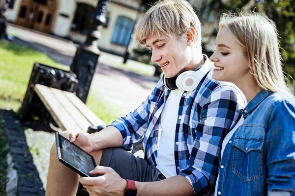 Amistosos estudiantes universitarios sonriendo y usando touchpad al aire libre — Foto de Stock